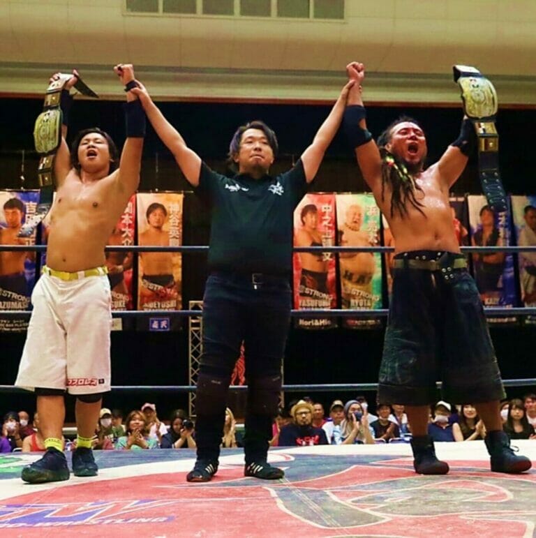 Un grupo de luchadores de BJW levantando las manos en el aire durante una lucha por equipos del Campeonato UWA.