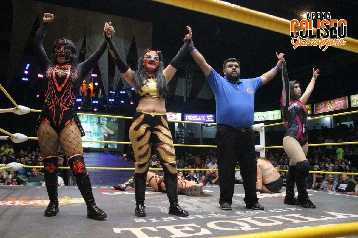 Un grupo de luchadores mostrando una mirada victoriosa con las manos en alto.