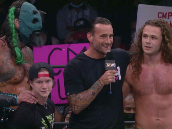 Un grupo de luchadores, incluidos CM Punk y Jack Perry, de pie con un micrófono frente a ellos.