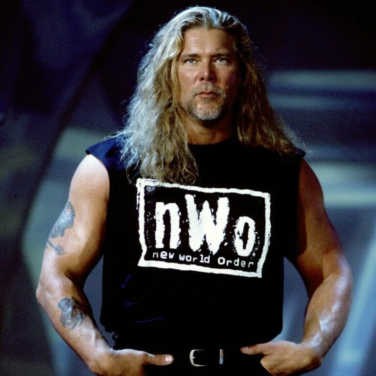 Un hombre con cabello largo y tatuajes llamado Kevin Nash parado frente a un escenario.