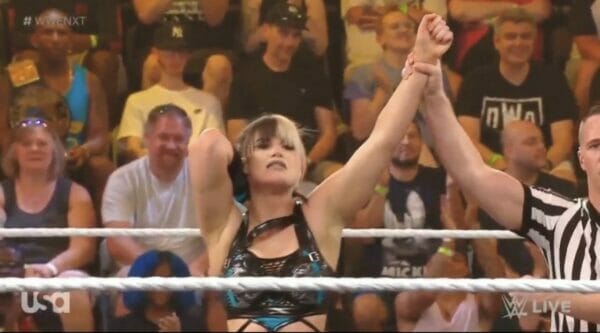 Una luchadora levanta triunfalmente el puño frente a una multitud que vitorea.