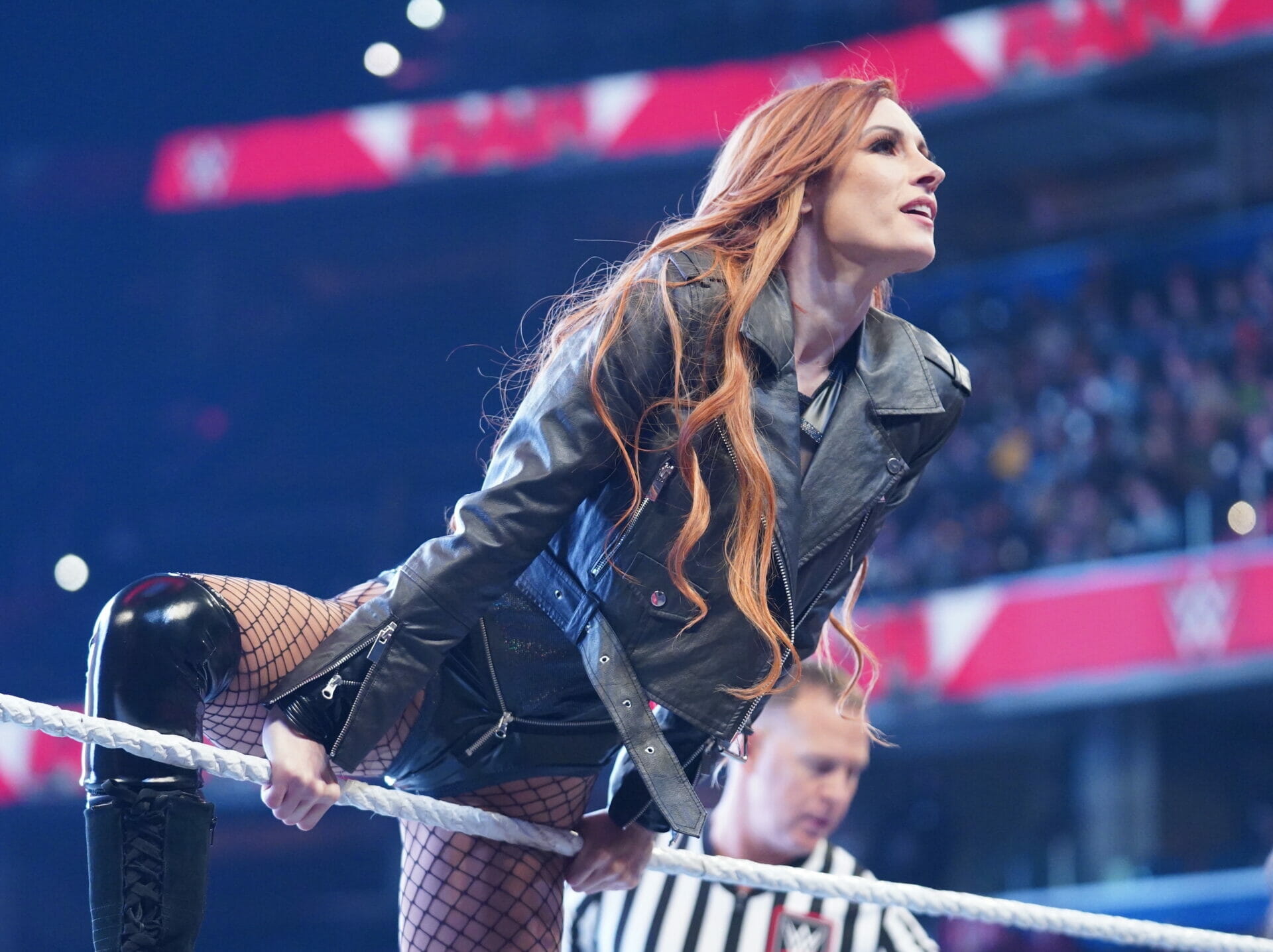 Una mujer con una chaqueta de cuero está de pie sobre una cuerda en un ring de lucha libre adornado con Los polémicos limones de Becky Lynch.