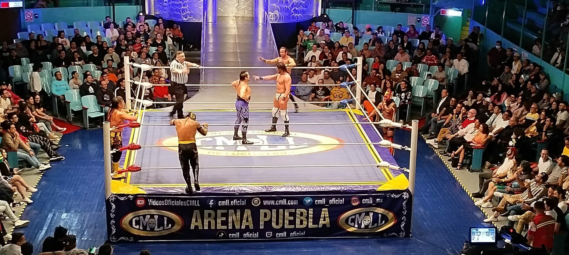 Un grupo de personas observando una pelea de lucha libre en una arena.