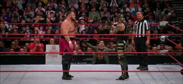 Dos luchadores en un ring con un árbitro.