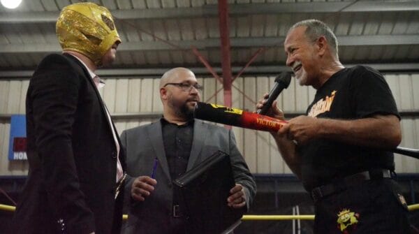 Superluchas - Un hombre de traje está hablando con otro hombre en un ring de lucha libre.