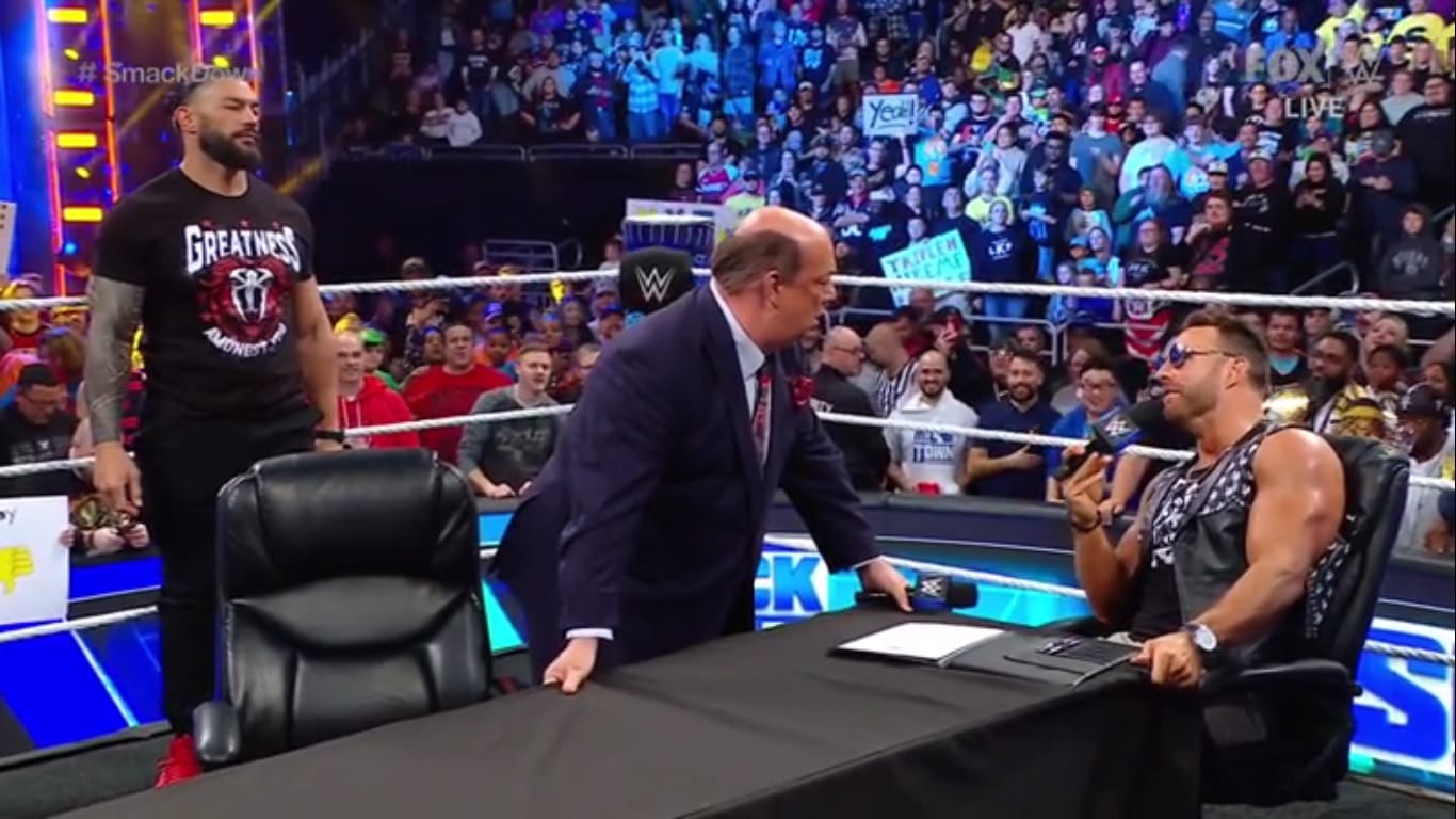 Superluchas - Los luchadores de la WWE Rey Mysterio y Santos Escobar sentados en una mesa frente a una multitud durante WWE SmackDown 27 de octubre de 2023.