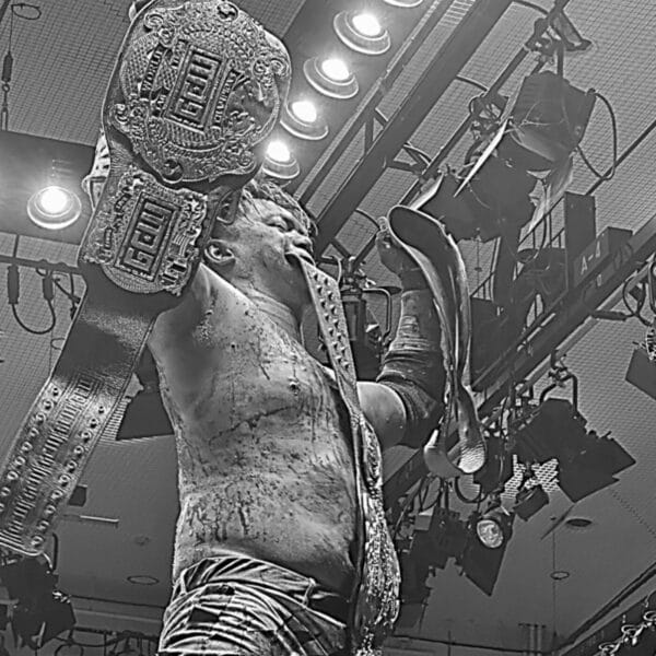 Superluchas - Toru Sugiura defiende su cinturón de campeonato, mostrando su fuerza y determinación en una poderosa fotografía en blanco y negro.
