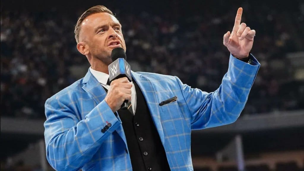Superluchas - Un hombre con traje azul, Nick Aldis, habla por un micrófono sobre su apertura a luchar en la WWE.
