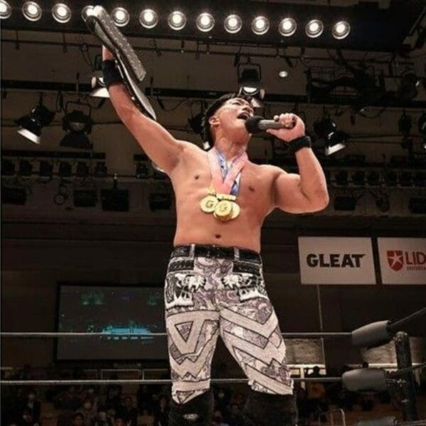 Superluchas - Un luchador GLEAT, T-Hawk, sostiene con confianza un micrófono en el ring de lucha libre como la firme monarca.