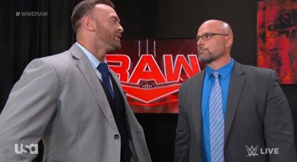 Superluchas - Dos hombres trajeados hablando frente a un cartel de WWE durante WWE RAW 23 de octubre 2023.