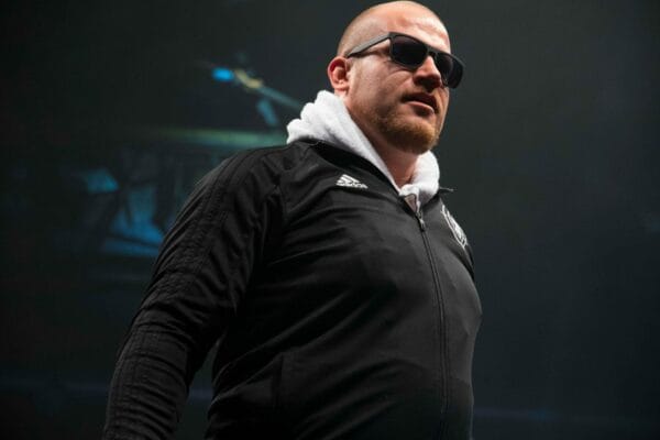 Superluchas - Un hombre con gafas de sol, Falleció Absolute Andy, de pie en un escenario.