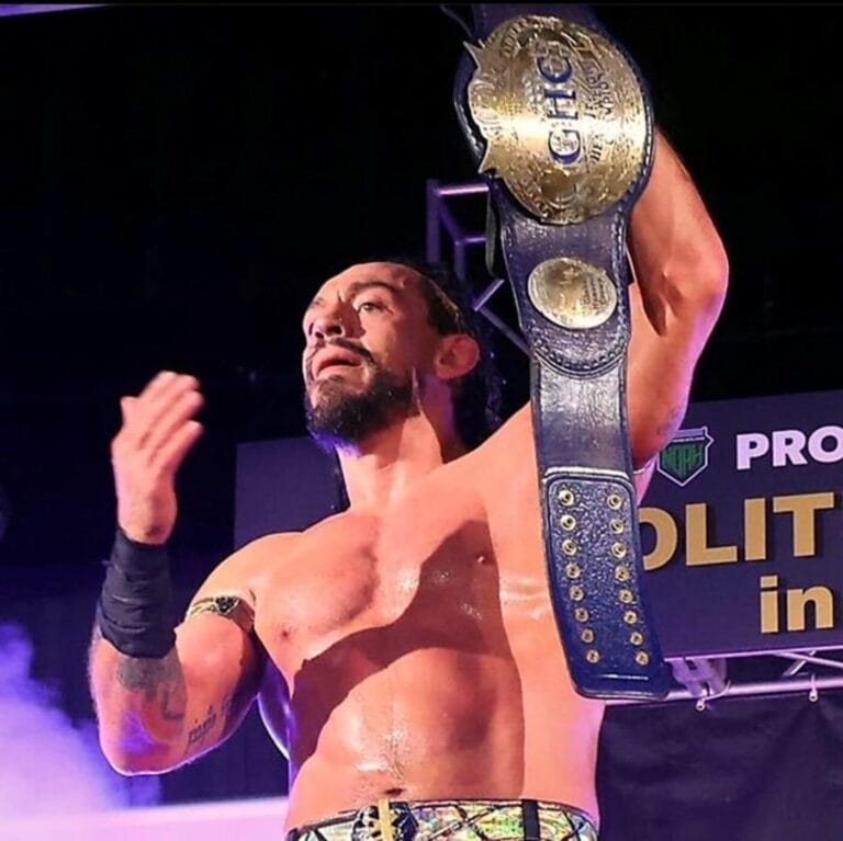 Superluchas - Un luchador mostrando con orgullo el cinturón de campeonato de NOAH en el escenario.