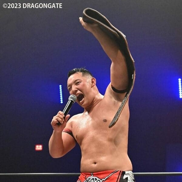 Superluchas - Madoka Kikuta, el actual campeón de Dragon Gate, sostiene con confianza un micrófono en la mano mientras se dirige a la multitud.
