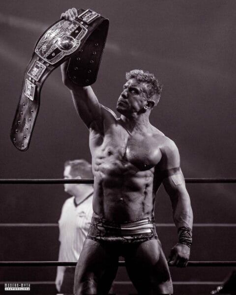 Superluchas - Un luchador victorioso en un ring de lucha libre, sosteniendo un cinturón de campeonato.