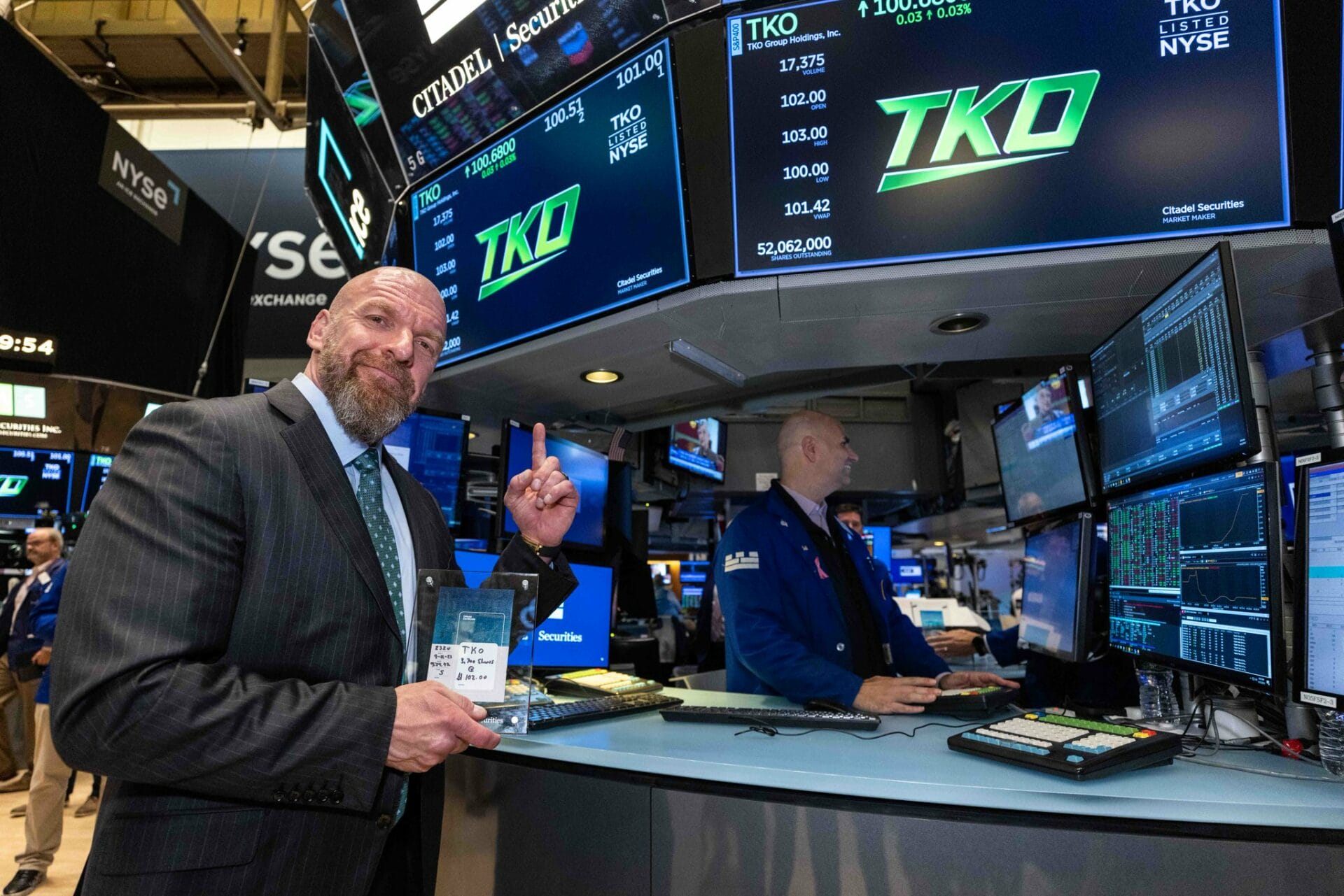 Superluchas - Triple H, vestido con un traje, se para con confianza frente a una bolsa de valores mientras proclama: "Endeavor es el siguiente nivel.