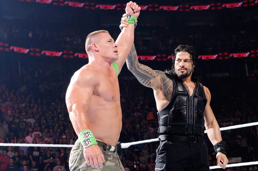 Superluchas - Dos luchadores, John Cena y Roman Reigns, uno al lado del otro en un ring.