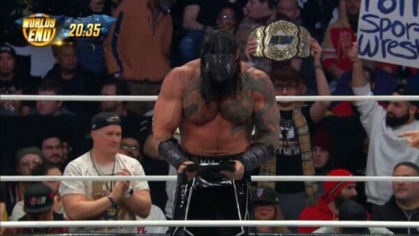 Superluchas - Killswitch, un luchador en un ring, sostiene triunfalmente un cartel frente a él.