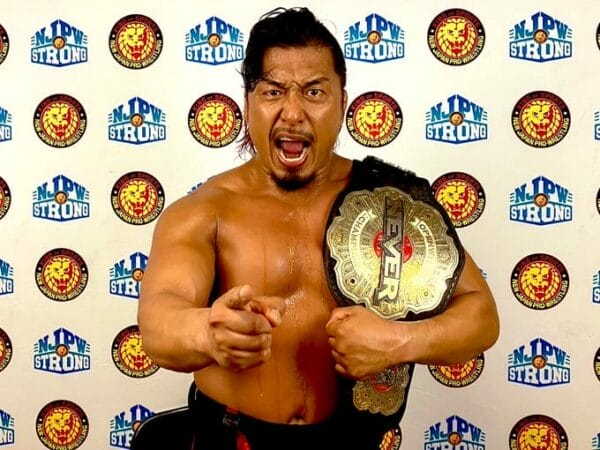 Superluchas - Shingo Takagi, un luchador, sosteniendo un cinturón de lucha libre frente a una pared.