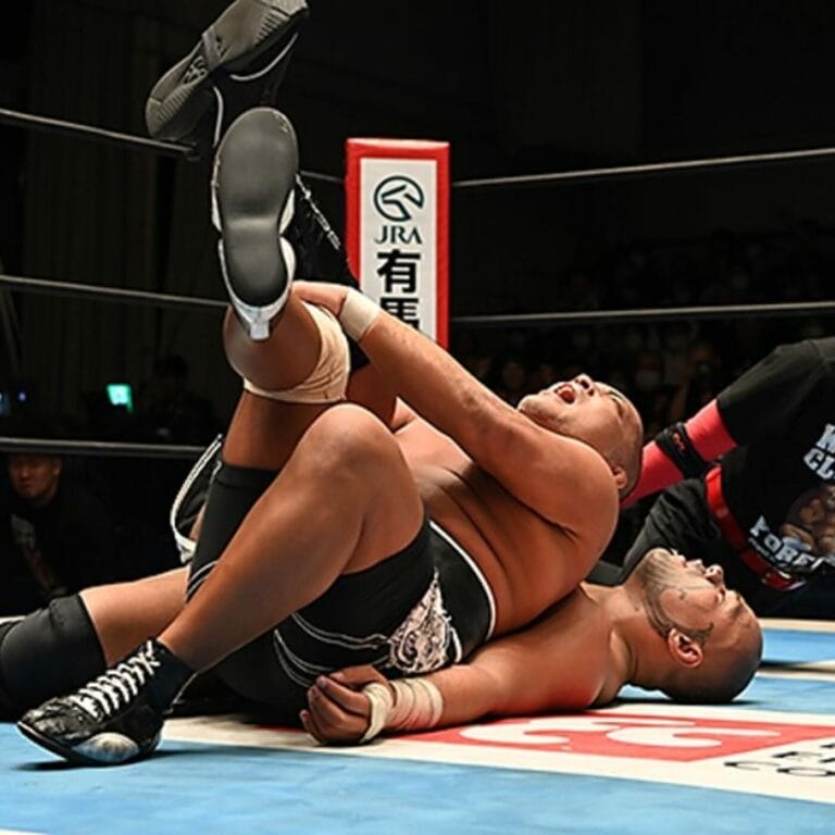 Superluchas - Un luchador yace en el suelo en un ring de lucha libre, en medio de la intensa acción de Defensas del cetro de tercias de NJPW y KOPW 23.