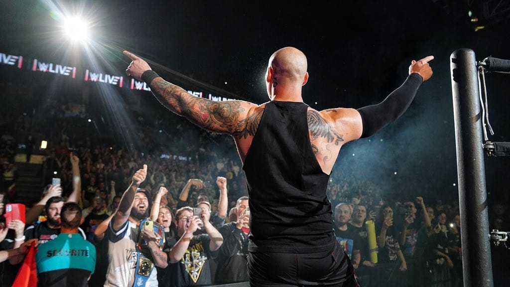 Superluchas - Un hombre con tatuajes parado frente a una multitud, que podría enfrentarse a Roman Reigns y Baron Corbin si los fanáticos lo apoyan.