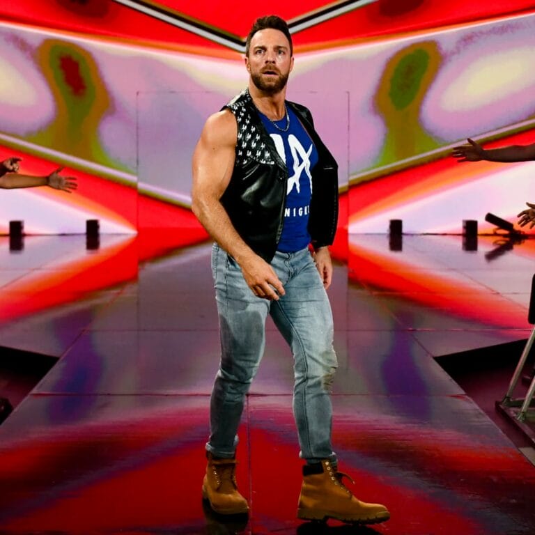 Superluchas - Un hombre con chaleco y jeans, LA Knight, de pie en un escenario durante la final.