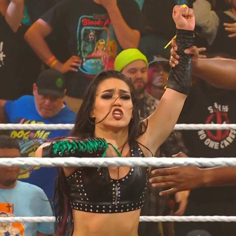 Superluchas - Roxanne Pérez, una mujer en un ring de lucha libre, levanta triunfalmente su puño, celebrando su victoria en el Campeonato de NXT.