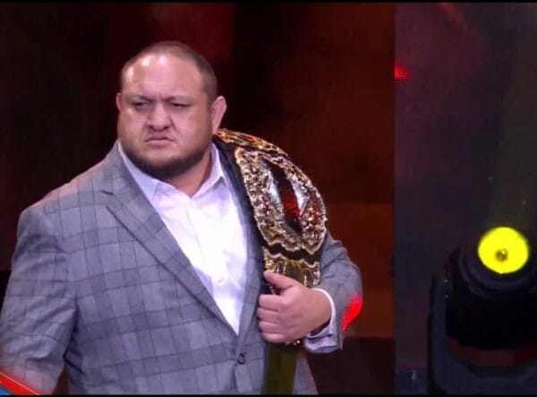 Superluchas - Un hombre de traje, sosteniendo el cinturón de lucha libre del Campeonato AEW.