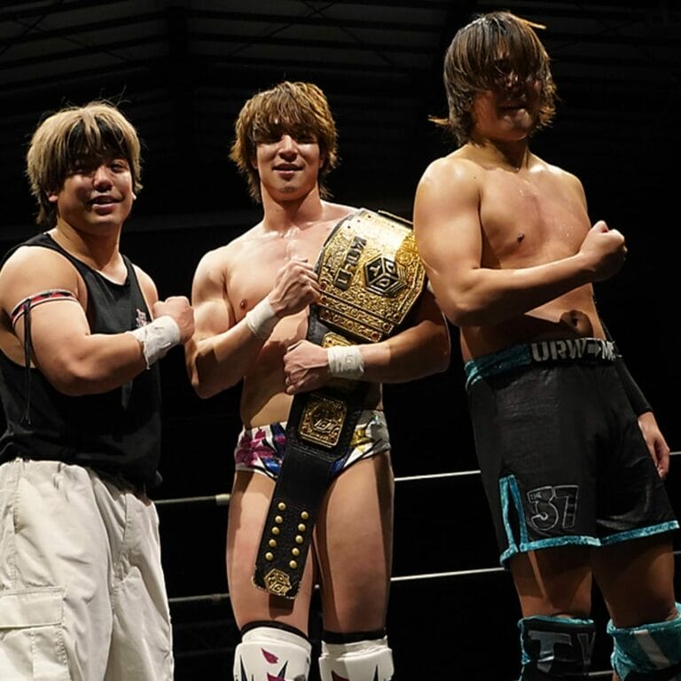 Superluchas - Tres luchadores realizando un movimiento de DDT en un ring de lucha libre.