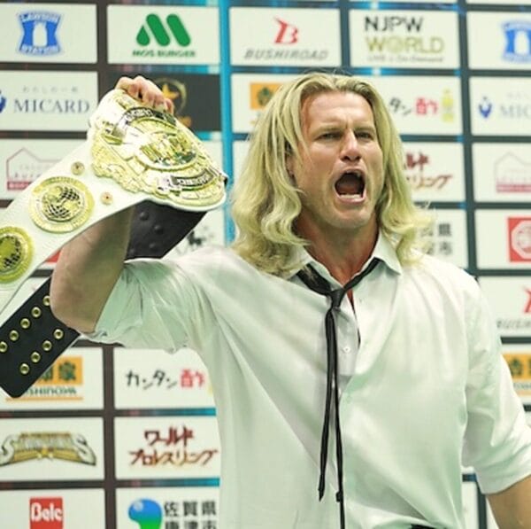 Superluchas - Nic Nemeth (Dolph Ziggler), un hombre de pelo largo, sostiene con orgullo el cinturón de lucha del Campeonato Global IWGP.