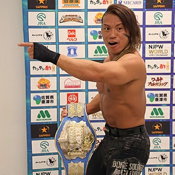 Superluchas - Un luchador de NJPW posando con su cinturón frente a una pared, listo para nuevos retos en New Year DASH!!