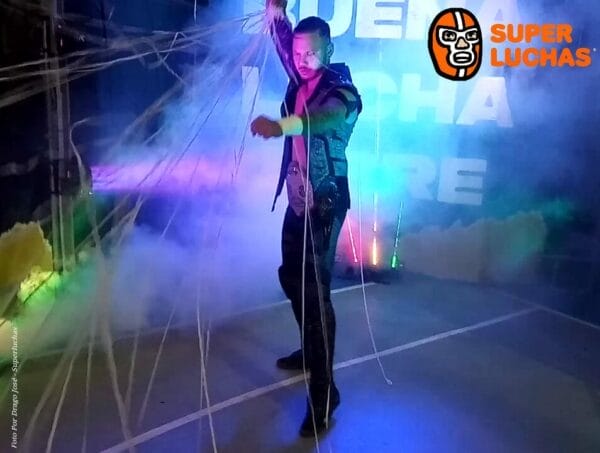 Superluchas - Un hombre con una chaqueta negra parado frente a una máquina de humo.